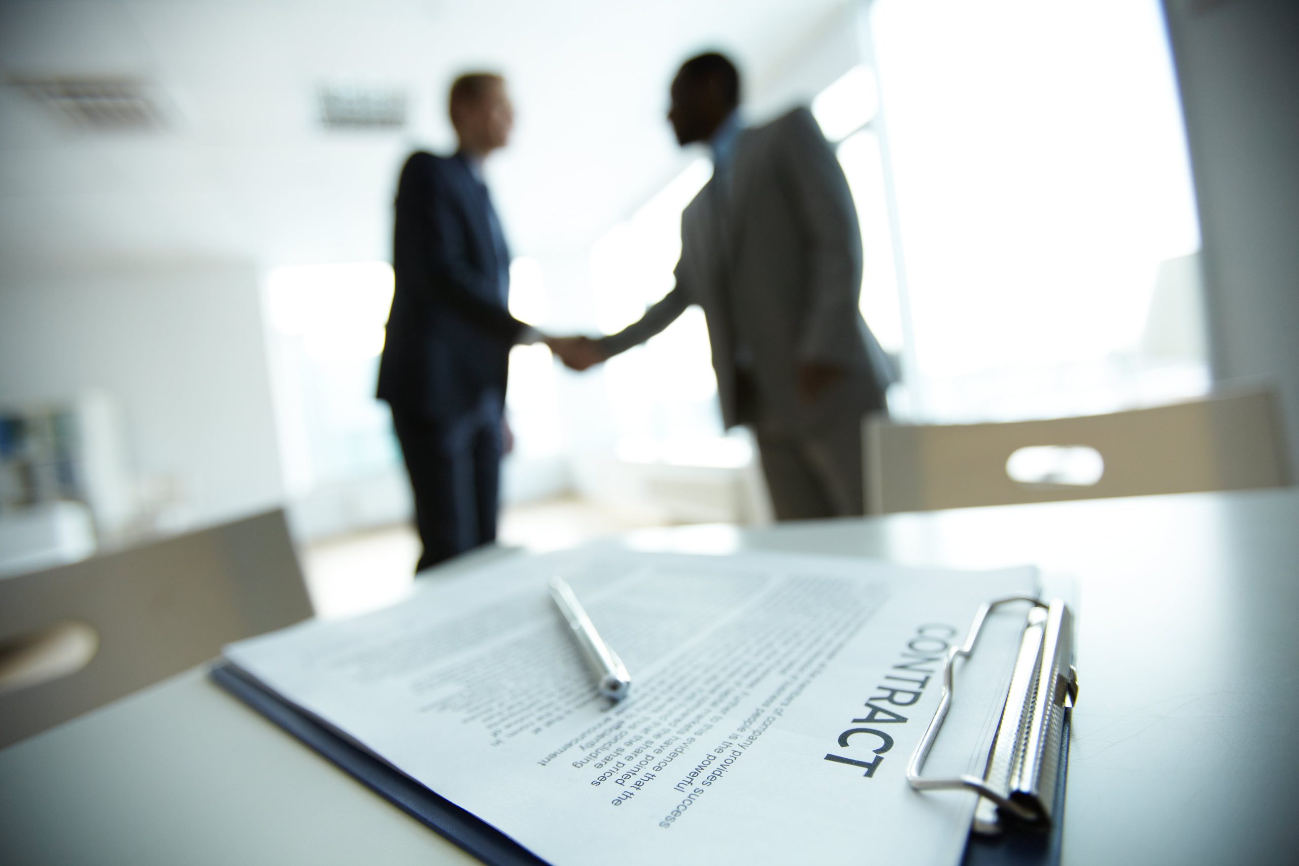 Image of business contract on background of two employees handshaking