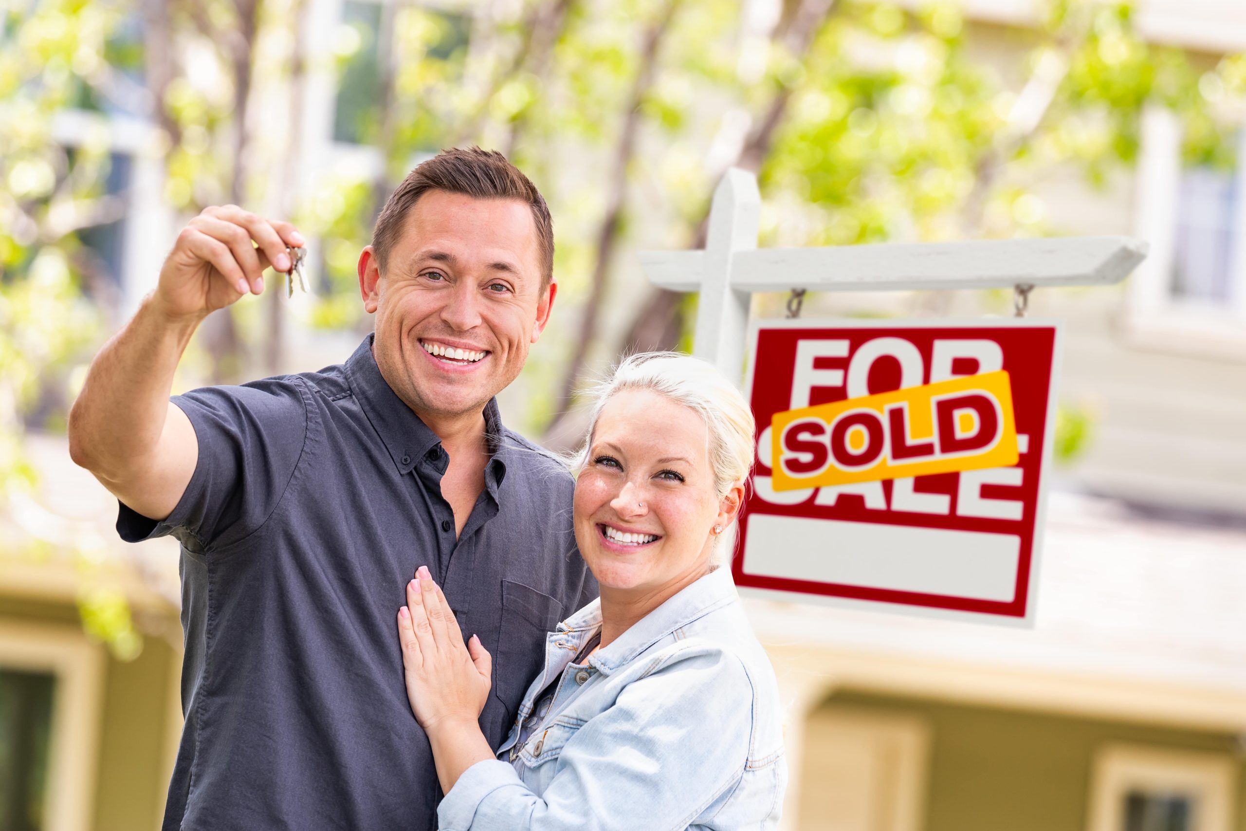 Couple in front of sold real estate sign and house with keys
